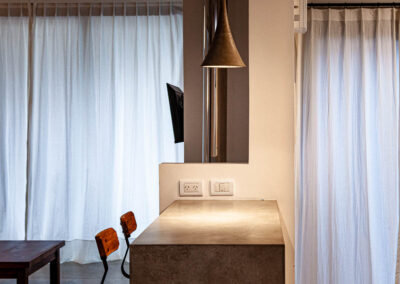 Detalle de la barra desayunadora de cemento alisado en Casa Moby Dick, con iluminación cálida y banquetas de madera.